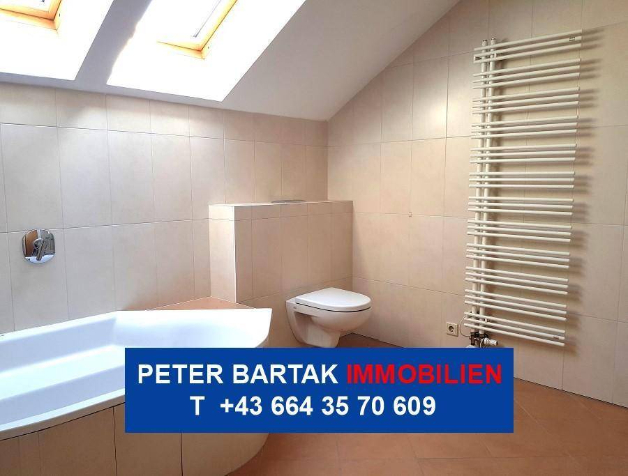 Helles Badezimmer im Dachgeschoss mit Fliesen, WC, Badewanne und Dachfenster für natürliches Licht.