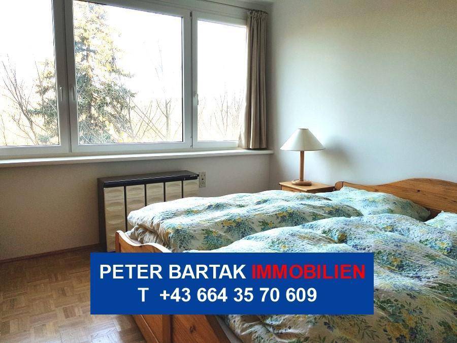 Helles Schlafzimmer mit Holzbett, Nachttisch und einem großen Fenster mit Blick ins Grüne.