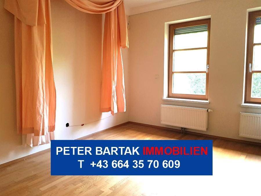 Gemütliches Schlafzimmer mit Parkettboden, zwei Fenstern und Vorhängen in warmem Pfirsichton.