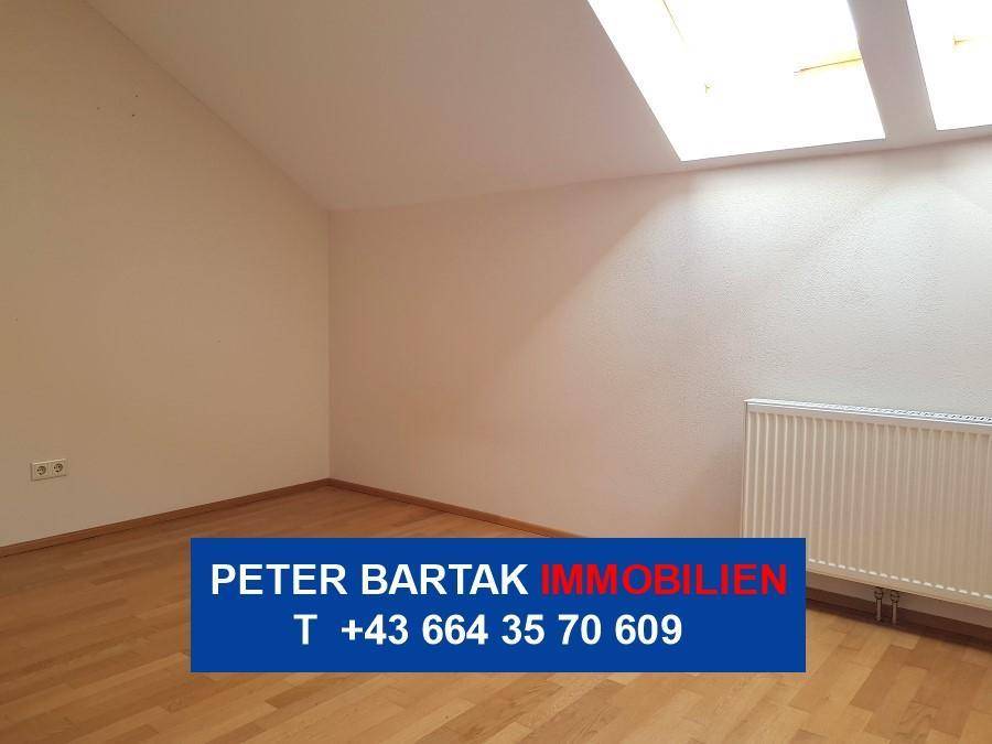 Helles Zimmer im Dachgeschoss mit Parkettboden, schräger Decke und zwei Dachfenstern.