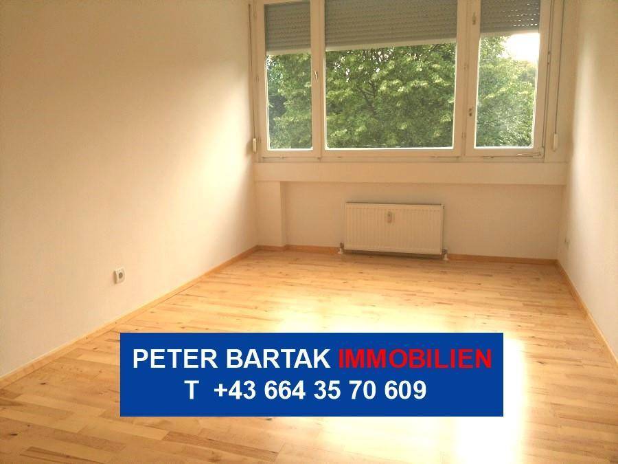 Helles Zimmer mit Parkettboden und großem Fenster, das viel Tageslicht hereinlässt und Grünblick bietet.
