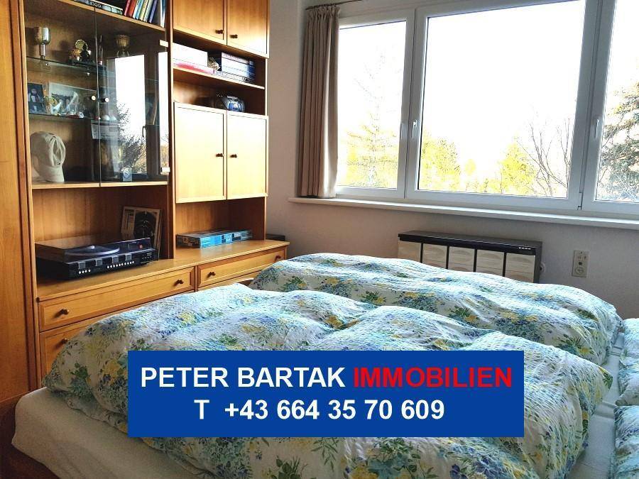Schlafzimmer mit Doppelbett, Bücherregal und einem großen Fenster, das viel Tageslicht spendet.