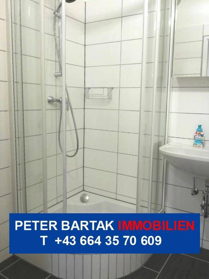 Modern geflieste Dusche mit Glasabtrennung und Duschkopf in einem hellen Badezimmer.