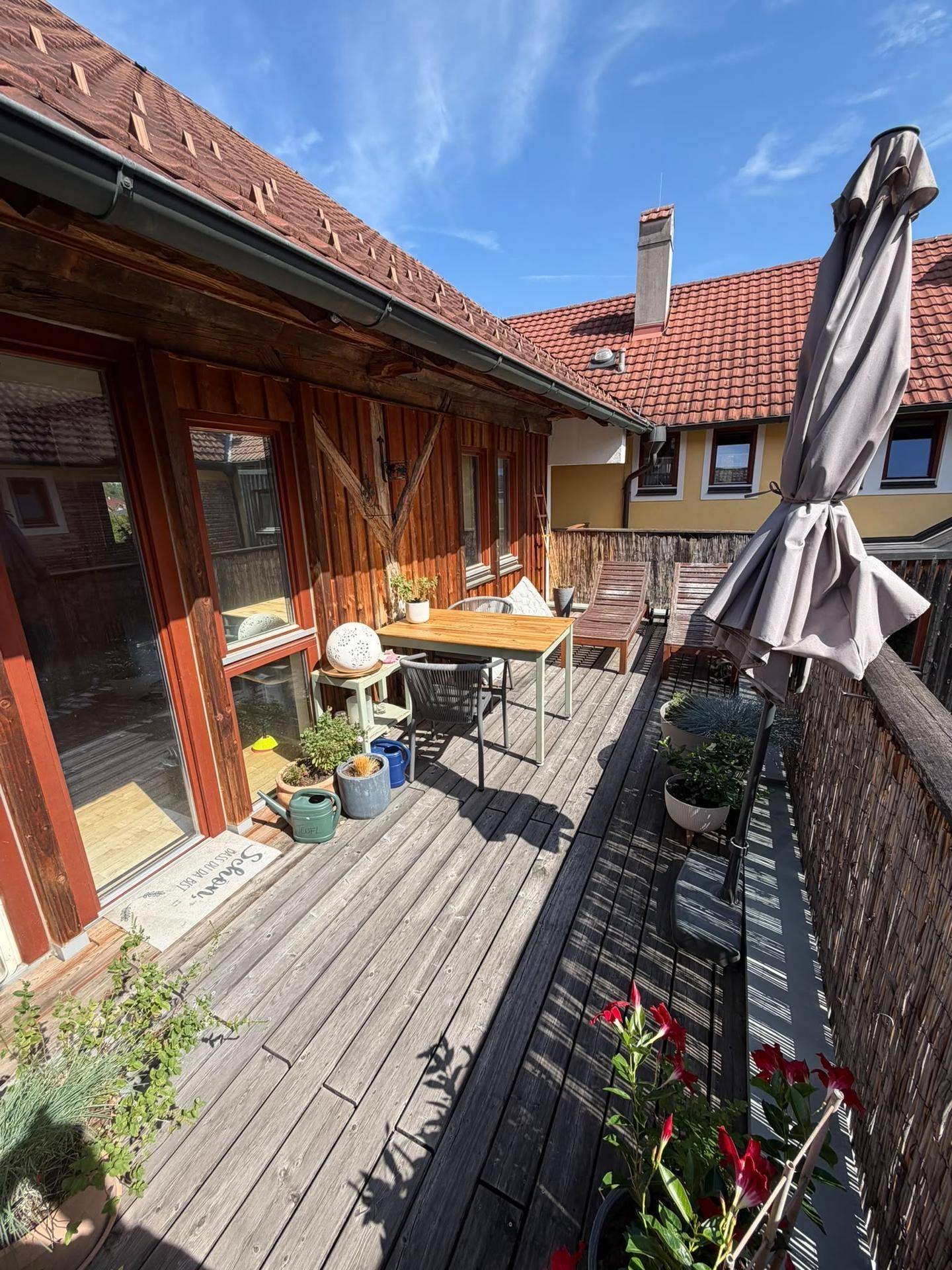 Großer Balkon mit Holzboden, Gartenmöbeln, Sonnenschirm und Pflanzen, perfekt für sonnige Tage.