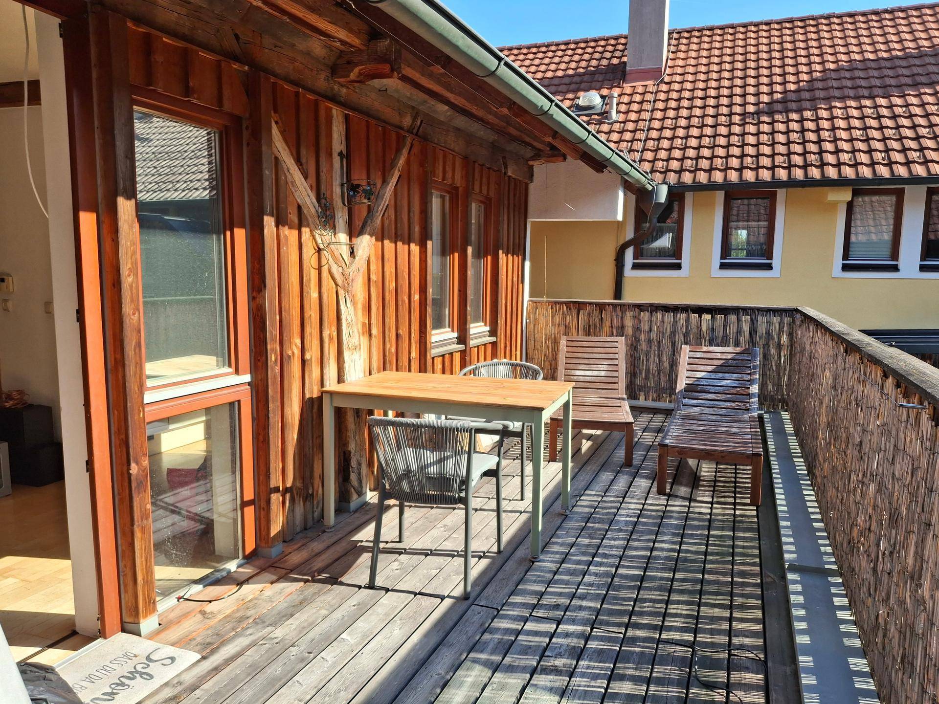 Sonniger Balkon mit Holzboden, Esstisch und Liegestühlen, ideal für entspannte Stunden im Freien.