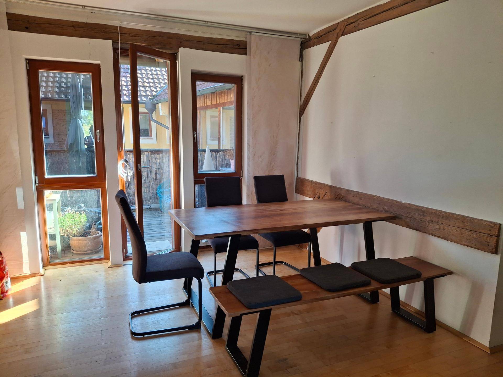 Heller Essbereich mit Holztisch, Sitzbank und Zugang zu einem Außenbereich, ergänzt durch sichtbare Holzbalken.