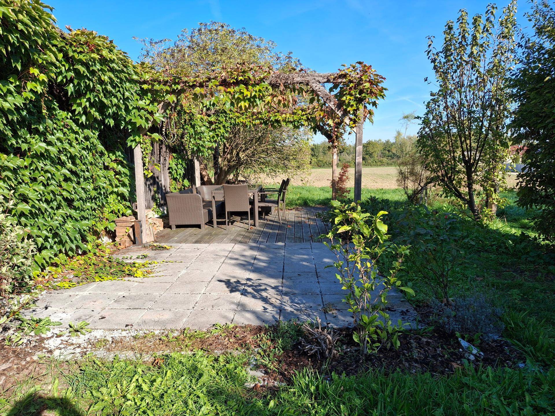 Geräumige Steinterrasse mit Pergola und Sitzgelegenheiten, umgeben von Natur und mit Blick auf Felder.