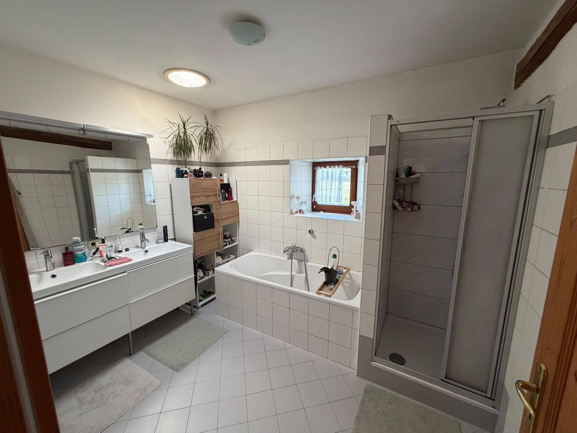 Helles Badezimmer mit Doppelwaschbecken, Badewanne und Duschkabine, ausgestattet mit Fliesen und einem Fenster.