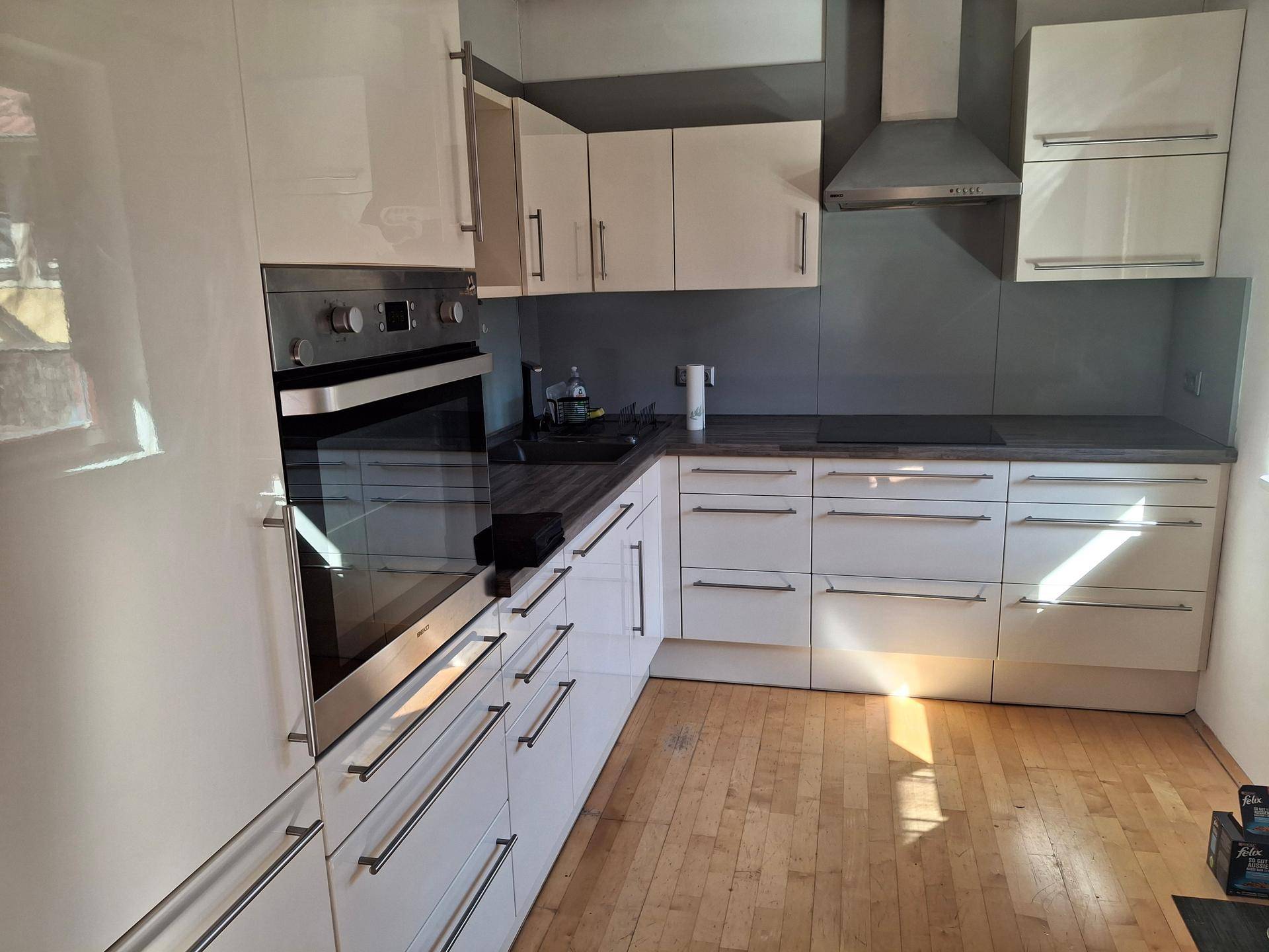 Moderne Küche mit weißen Hochglanzfronten, integriertem Backofen und Induktionskochfeld, sowie Holzboden.