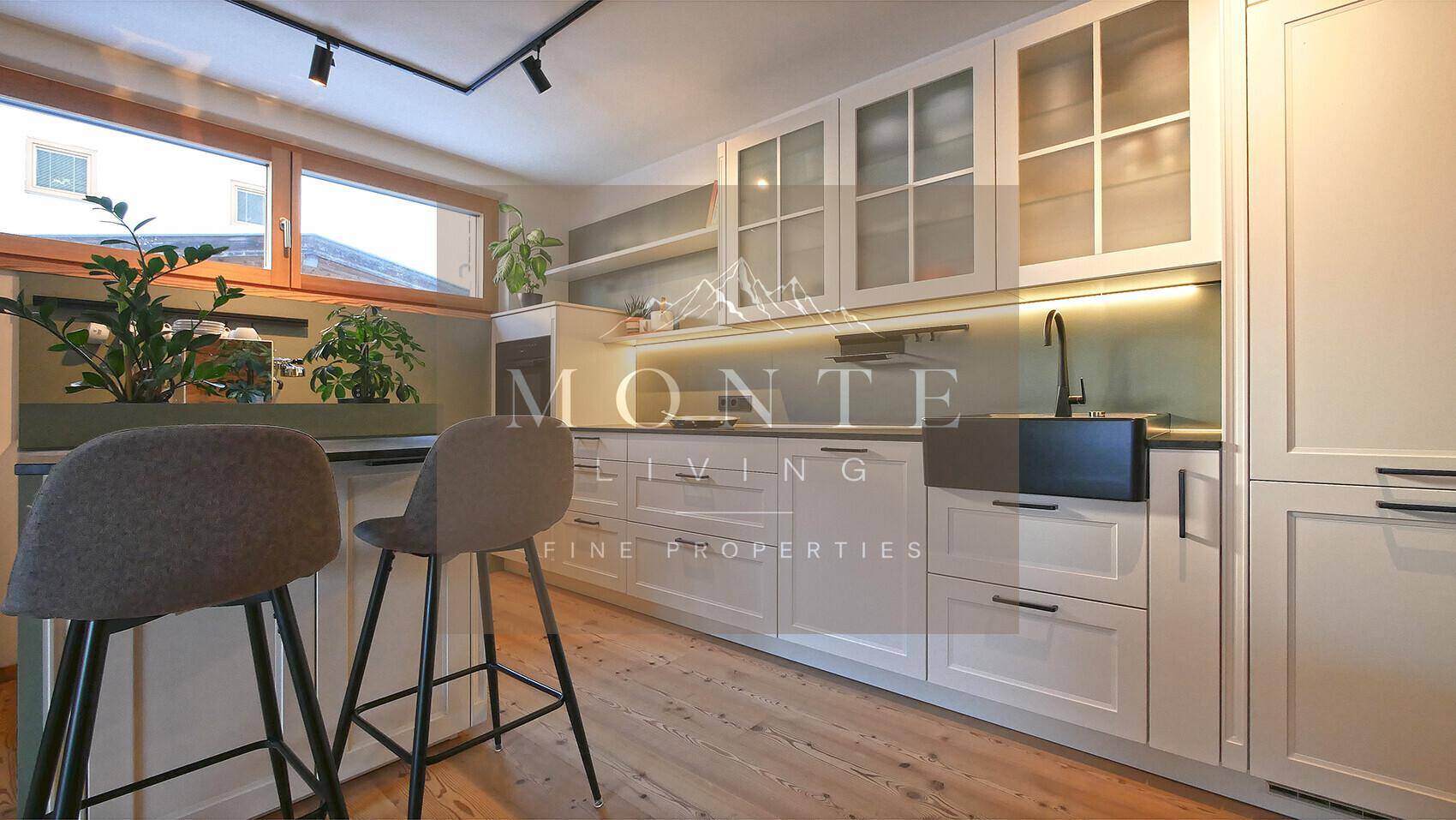 Moderne weiße Einbauküche mit Frühstücksbar, dunkler Arbeitsplatte und integrierten Geräten.