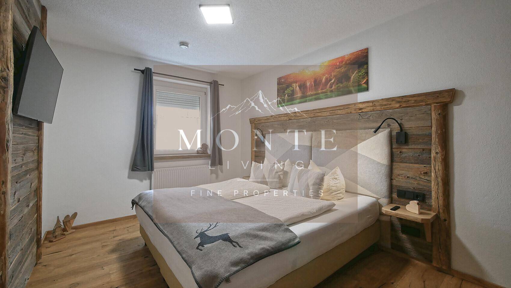 Gemütliches Schlafzimmer mit rustikalem Holzbett, Holzboden und Wandfernseher.