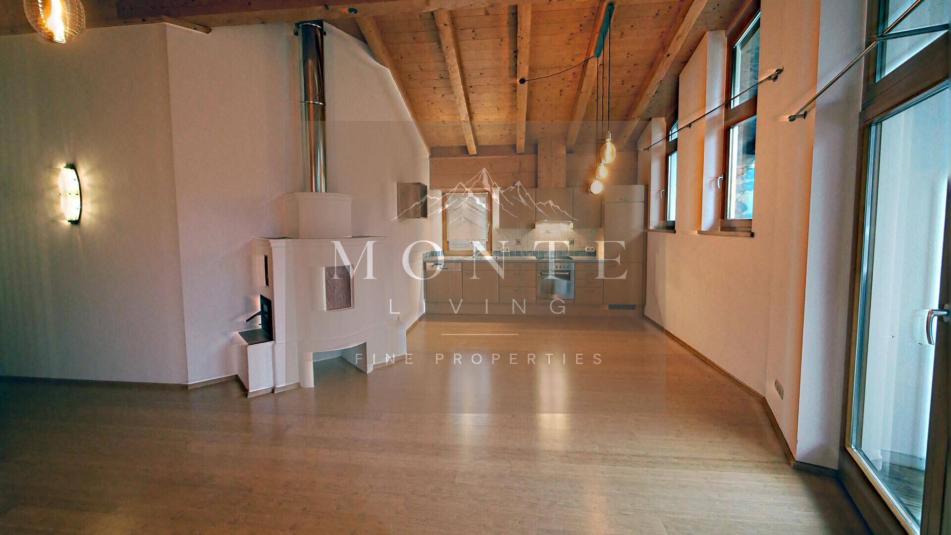 Geräumiger Wohnbereich mit Holzbalken, Parkettboden und Zugang zu einem Balkon oder einer Terrasse.