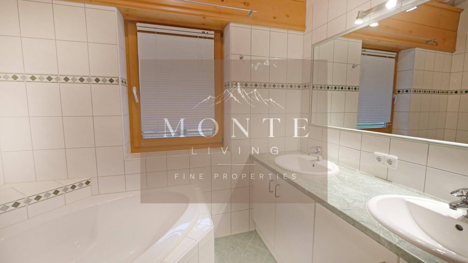 Helles Badezimmer mit Badewanne, Doppelwaschbecken und Fliesen in neutralen Farben.