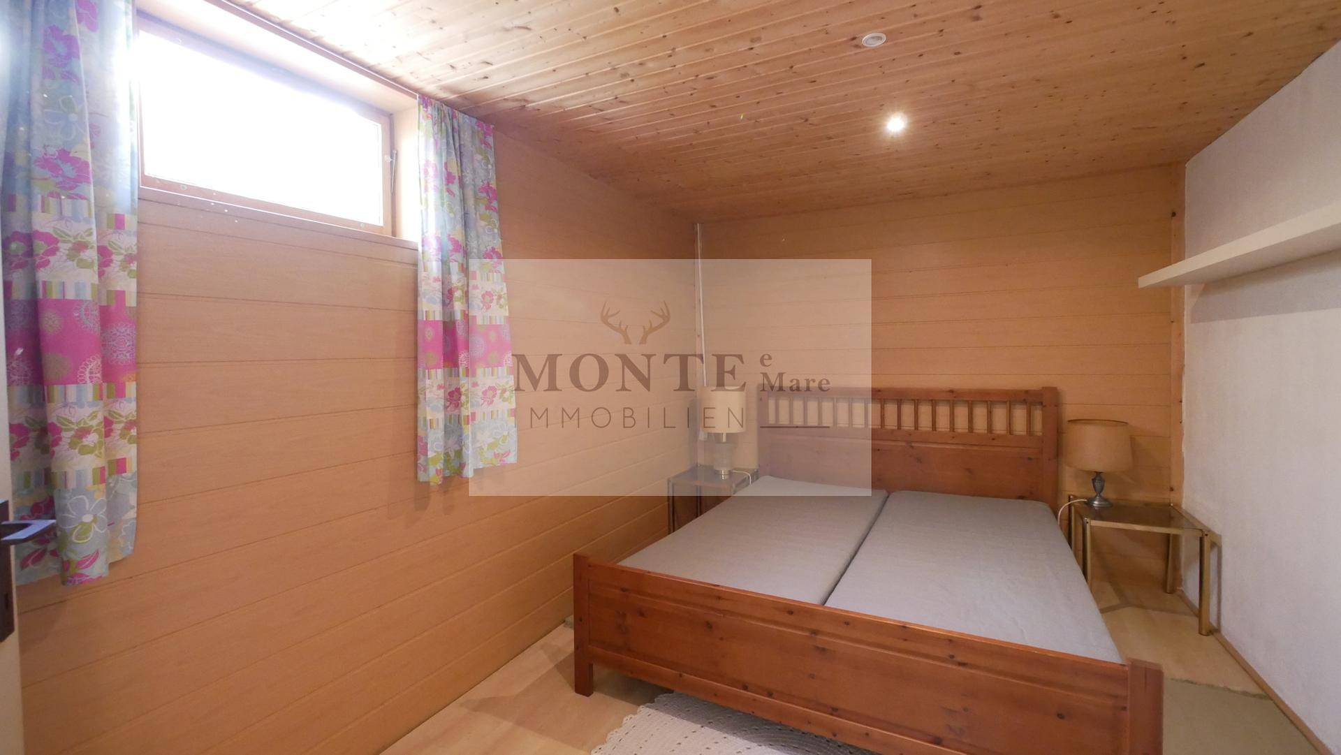 Gemütliches Schlafzimmer mit Holzwänden, Doppelbett und Dachschrägenfenster.