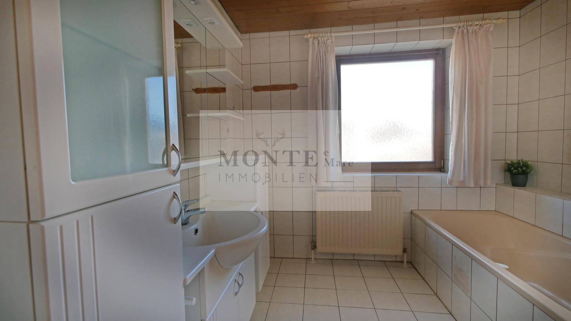 Gefliestes Badezimmer mit Badewanne, Waschbecken und Fenster für Tageslicht.