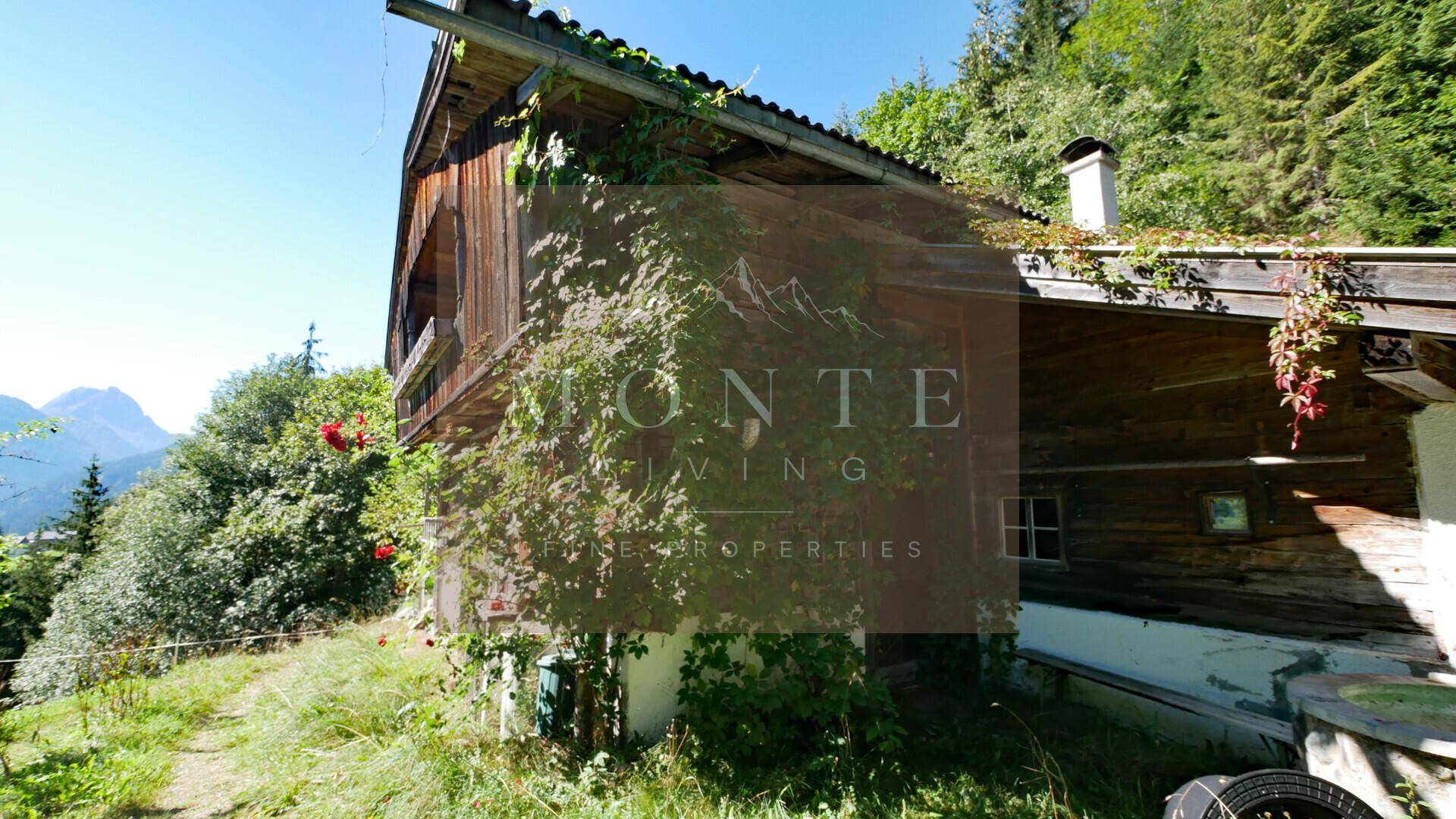 Seitenansicht eines traditionellen Holzhauses mit bewachsenen Wänden und einem Schornstein unter blauem Himmel.