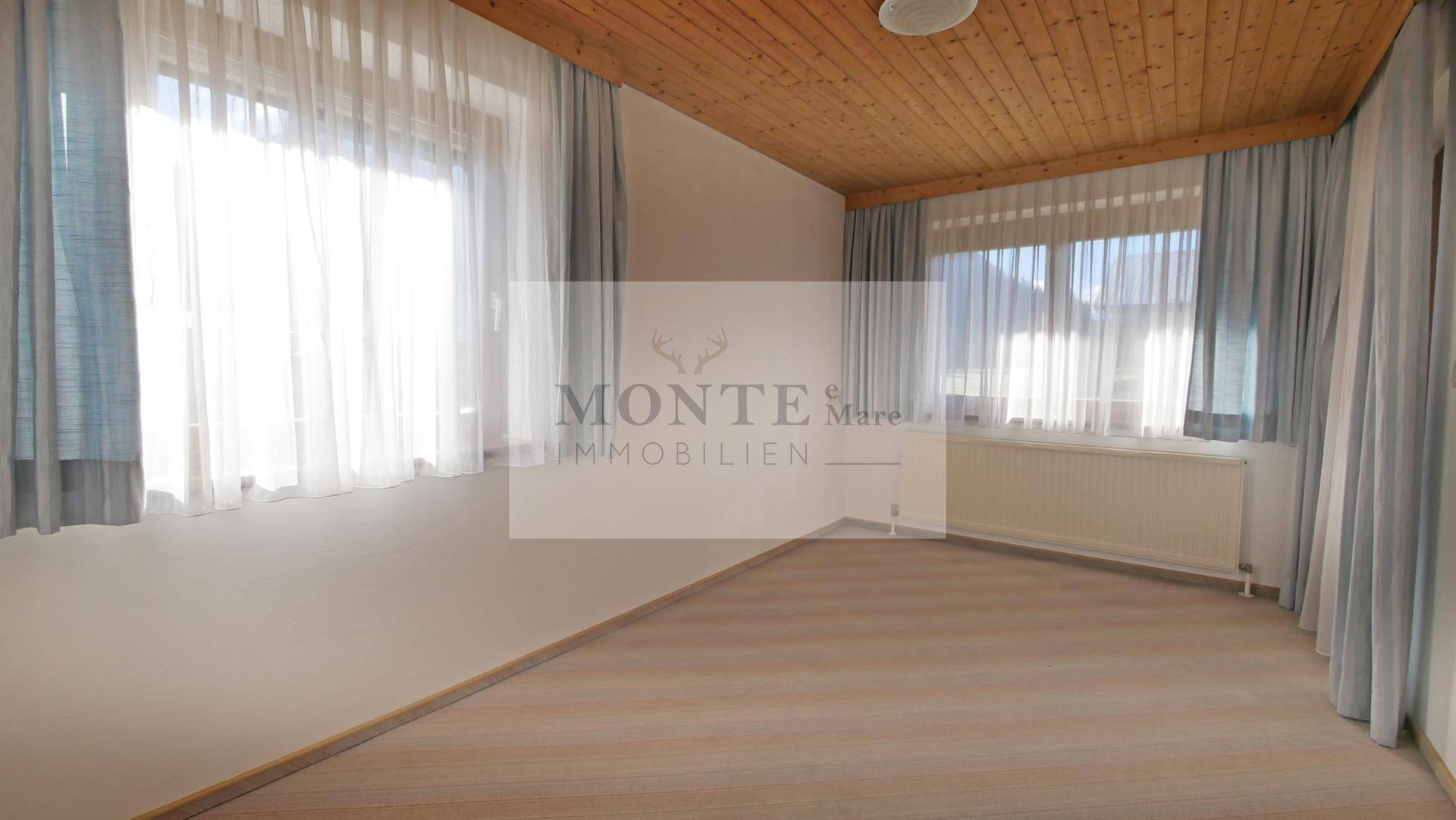 Geräumiges Schlafzimmer mit Holzdachschräge, großen Fenstern und viel Tageslicht.