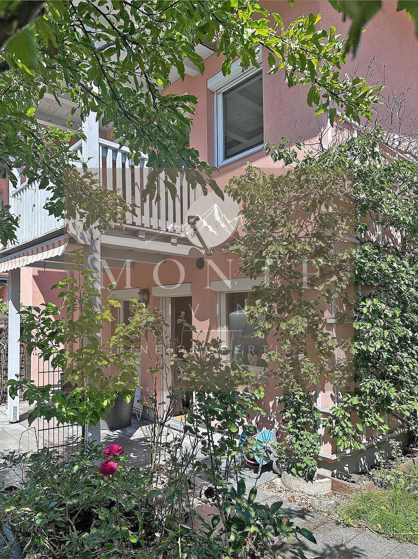 Rosa gestrichene Hausfassade umgeben von üppigem Grün und Bäumen mit einem kleinen Balkon.