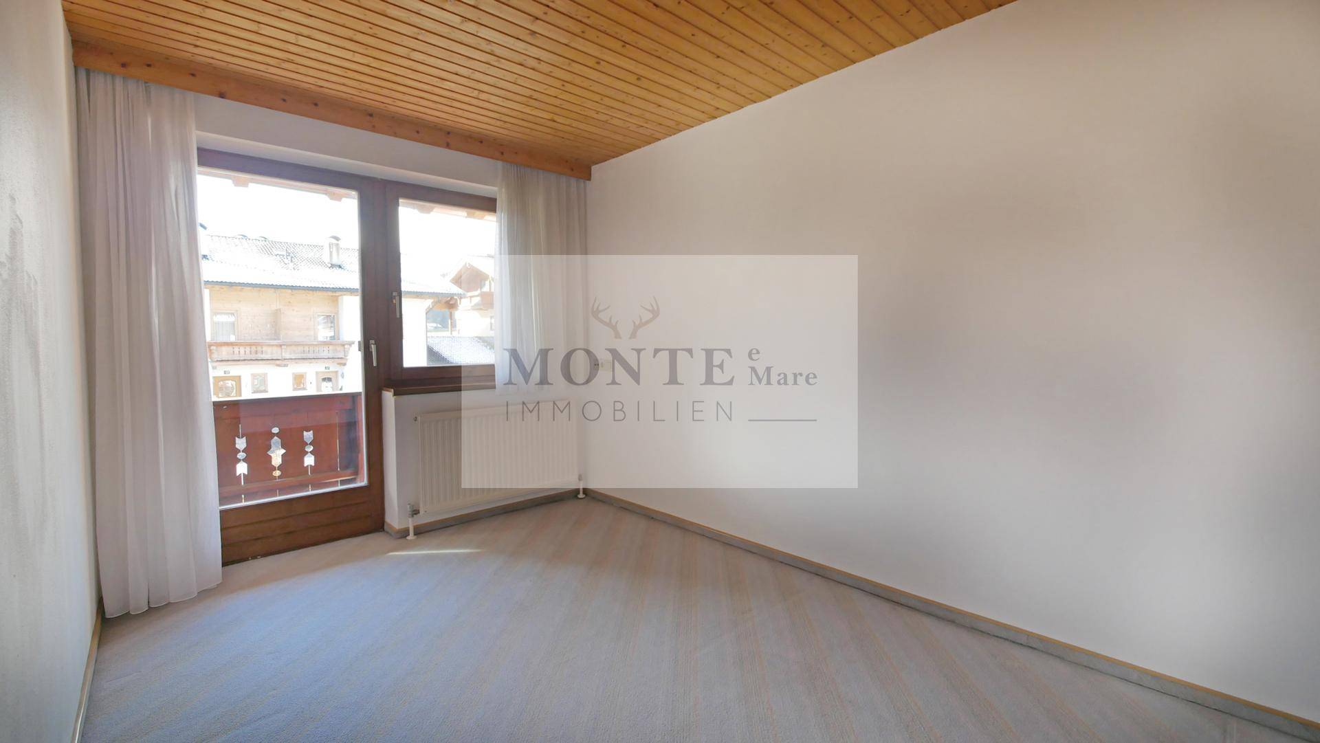 Schlafzimmer mit Zugang zum Balkon, Holzdachschräge und hellem Boden.