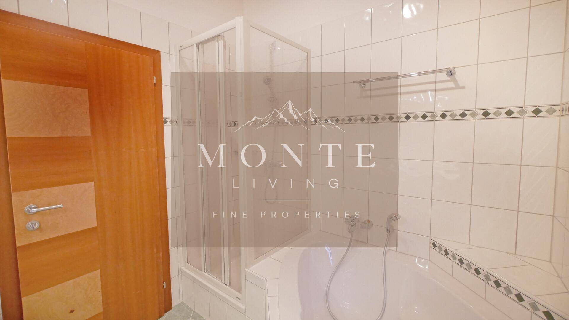 Badezimmer mit Badewanne, Duschkabine und weißen Fliesen mit dekorativer Bordüre.