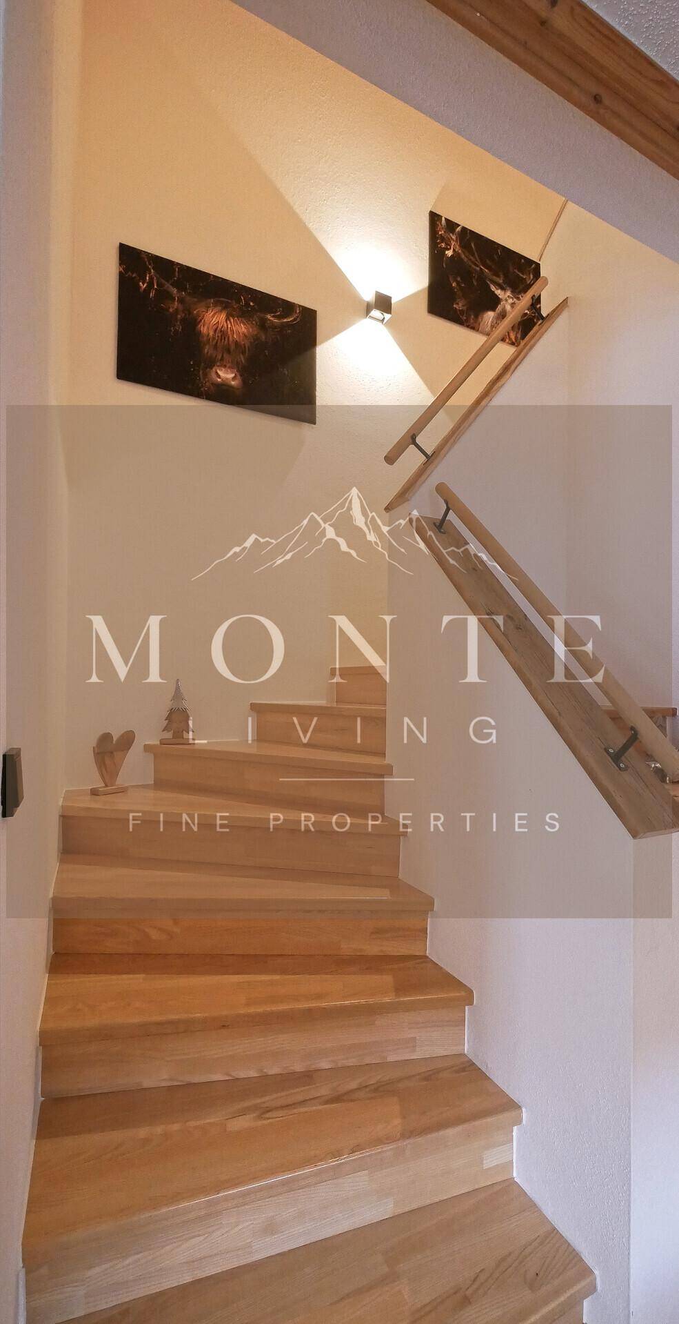 Holztreppe mit modernen Wandbildern und indirekter Beleuchtung im Flurbereich.