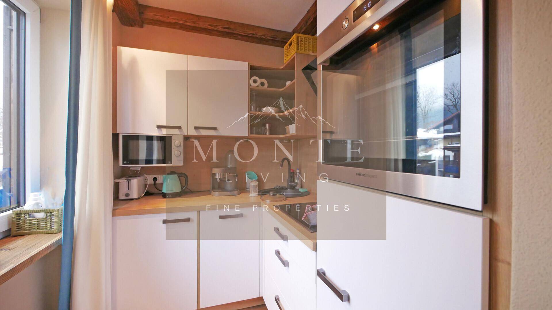 Kompakte Einbauküche mit weißen Schränken, Holztheke und integrierten Geräten sowie Fenster.