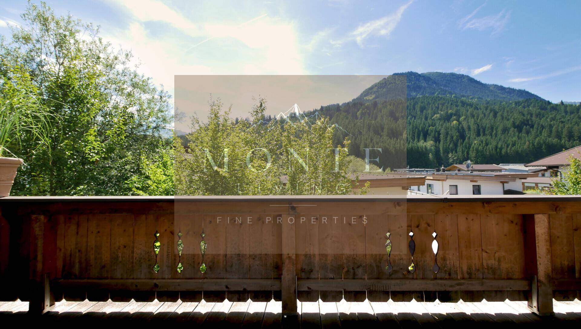 Sonniger Balkon mit traditionellem Holzgeländer und weitem Blick auf die umliegende Berglandschaft.