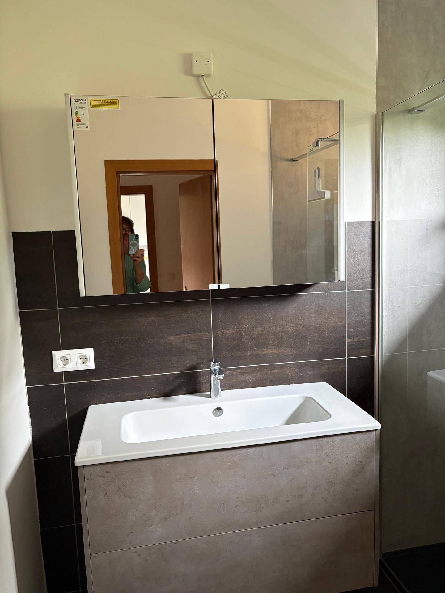 Modernes Badezimmer mit Waschtisch, Spiegelschrank und dunklen Fliesen an den Wänden.