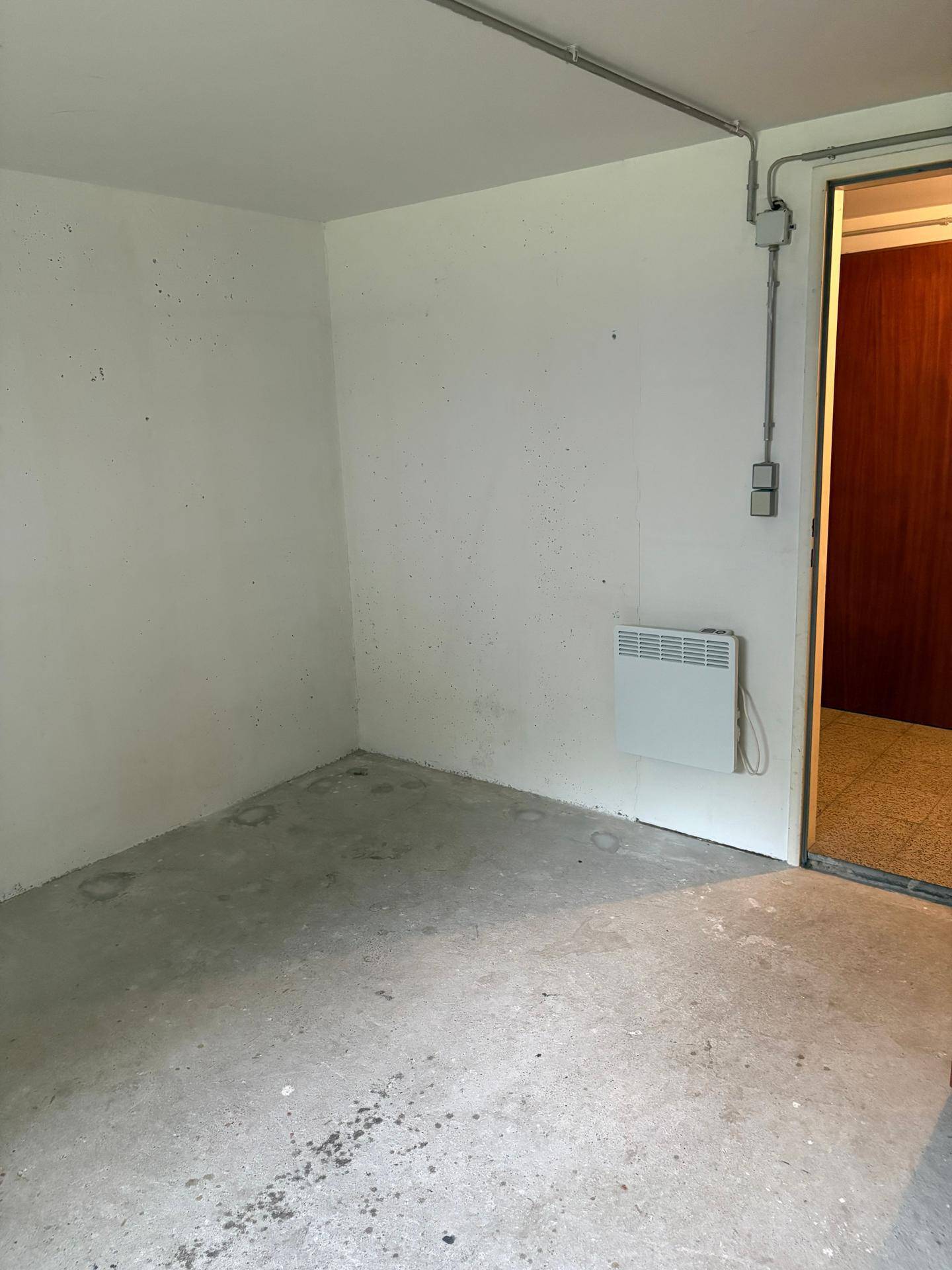 Leerer Kellerraum mit Betonboden, weiß gestrichenen Wänden und einem Wandheizkörper.