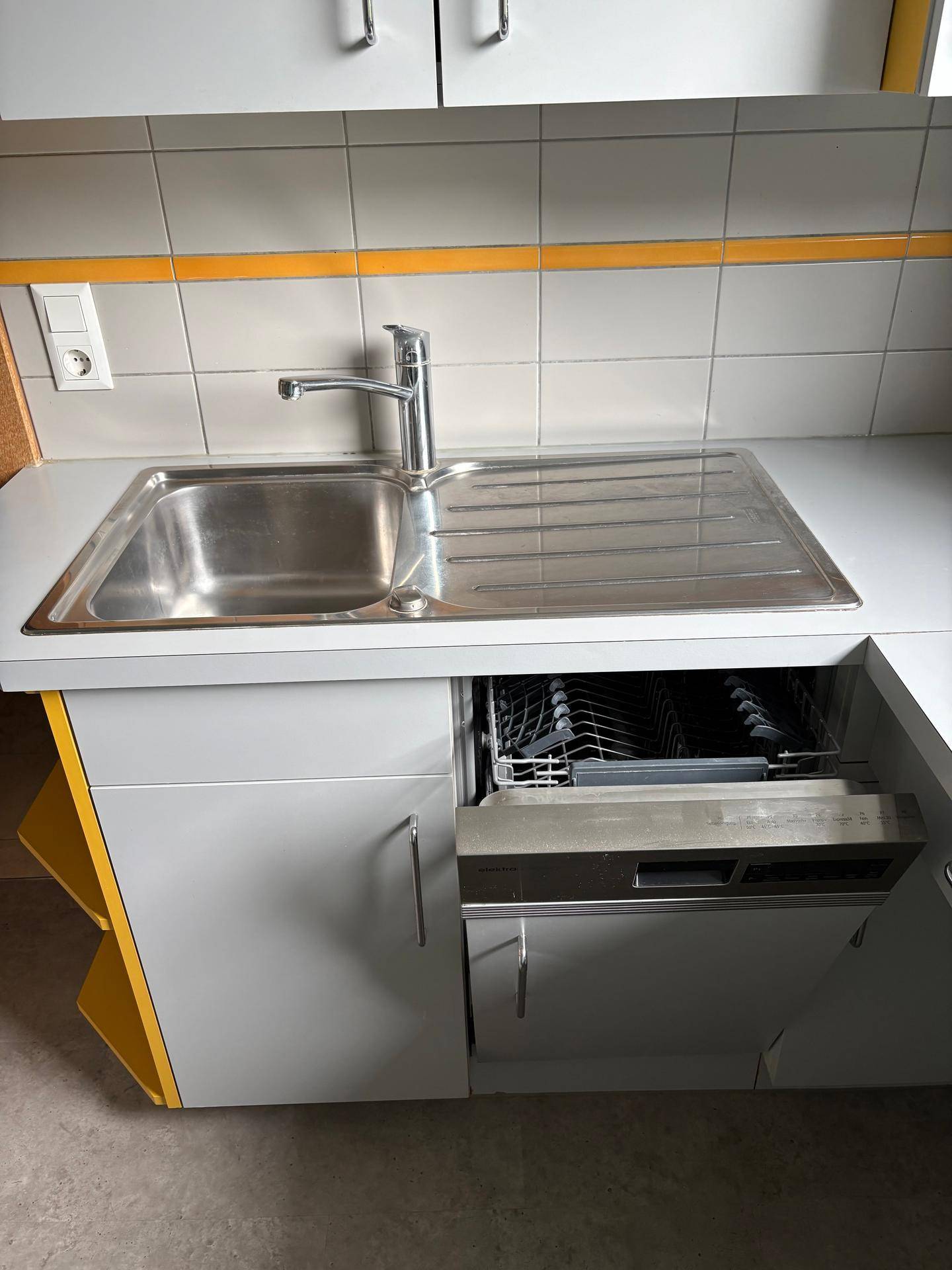 Küchenzeile mit Spülbecken aus Edelstahl, grauer Arbeitsplatte und integriertem Geschirrspüler.