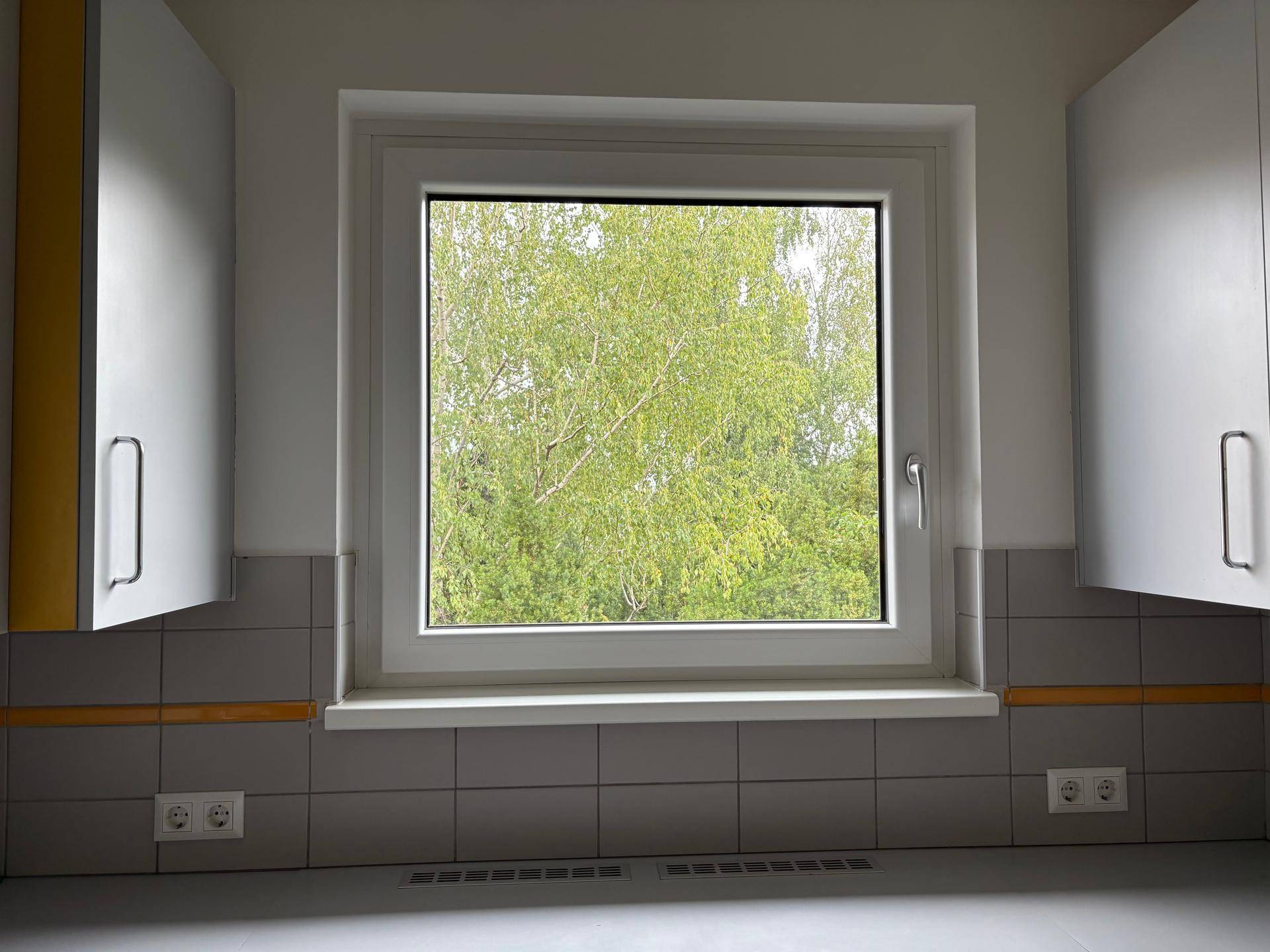 Helle Küche mit Fenster und Blick ins Grüne, umgeben von weißen Küchenschränken.