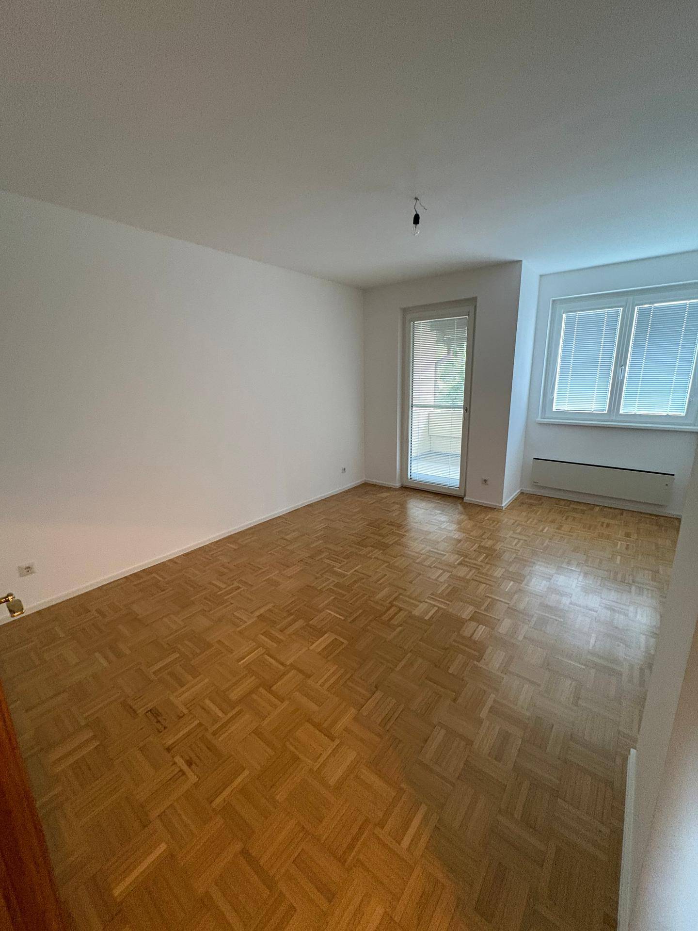 Helles Wohnzimmer mit klassischem Parkettboden und großem Fenster mit Balkonzugang.