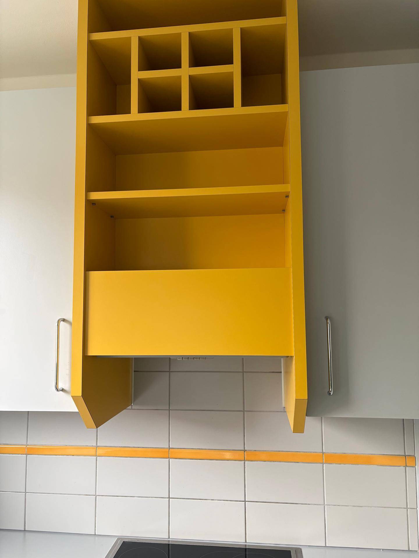 Moderne Küche mit auffälligem gelbem Regal über dem Kochfeld und weißen Unterschränken.