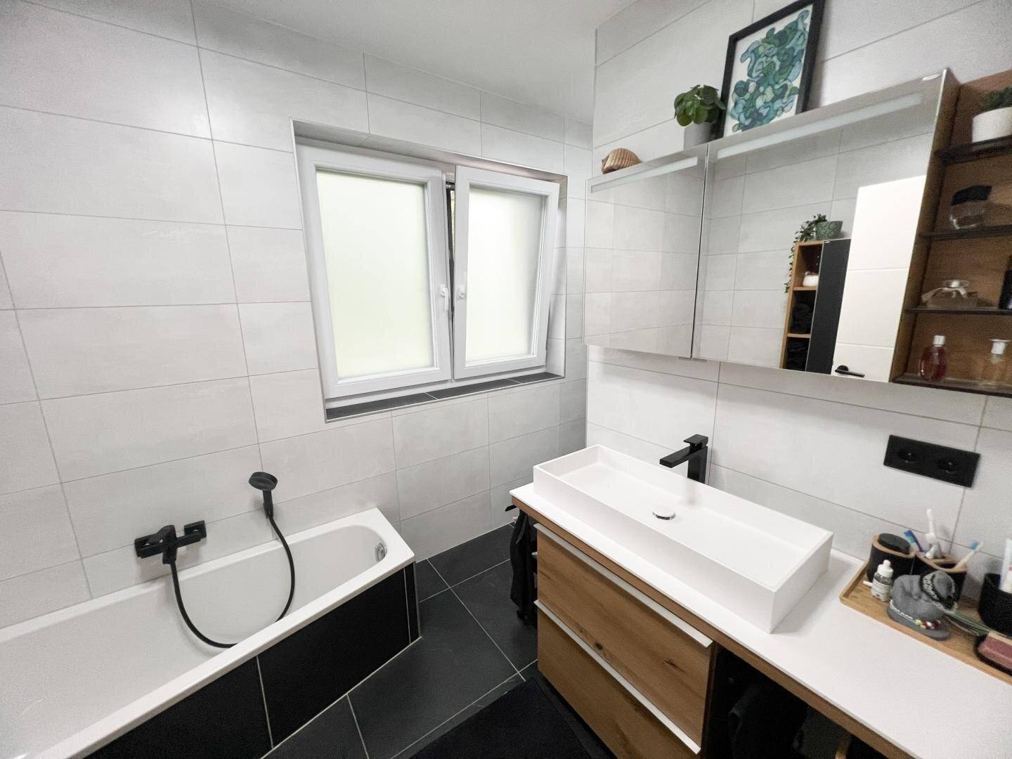 Modernes Badezimmer mit Badewanne, Waschbecken und Fenster für natürliche Belüftung und Licht.