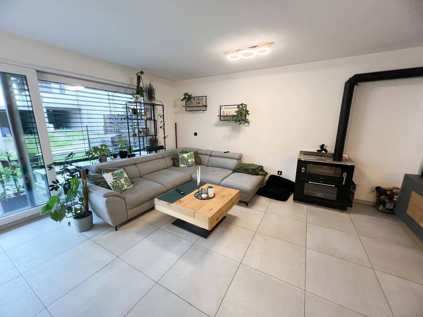 Gemütliches Wohnzimmer mit großem Ecksofa, Kaminofen und Zugang zu einem sonnigen Außenbereich.