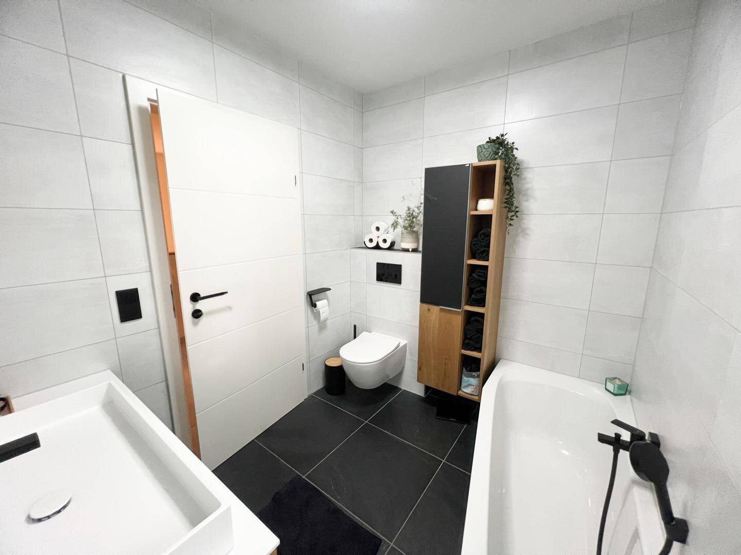 Modernes Badezimmer mit Badewanne, Wand-WC und stilvollen Holz- und Schwarzakzenten.