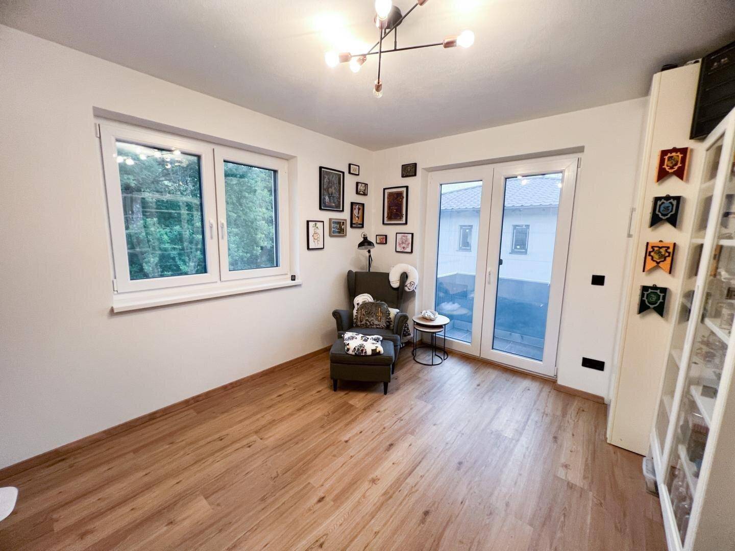Helles Zimmer mit Holzboden, großen Fenstern und Zugang zu einem Balkon.