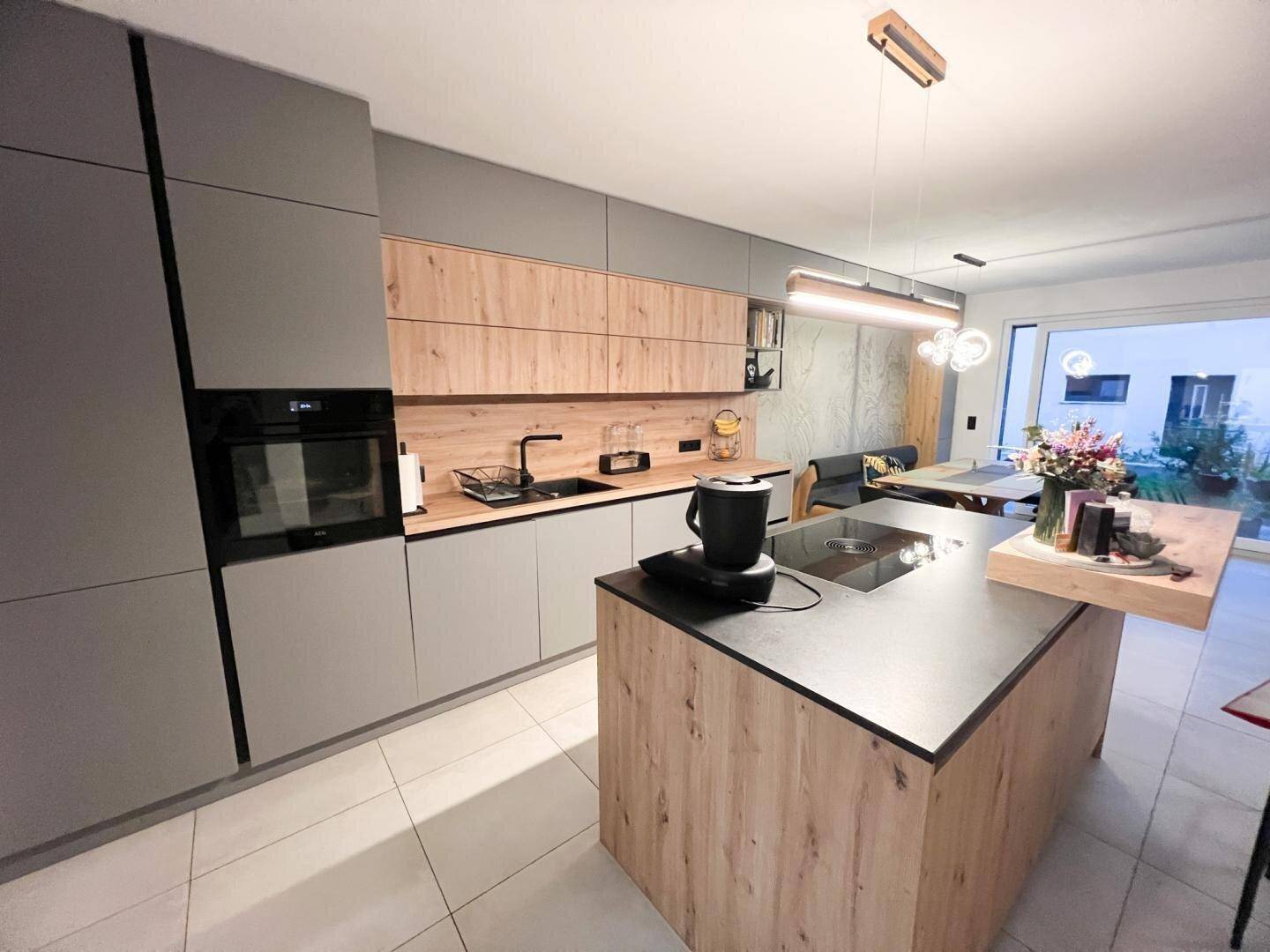 Moderne Küche mit grauen und holzfarbenen Fronten, Kochinsel und integrierten Geräten.