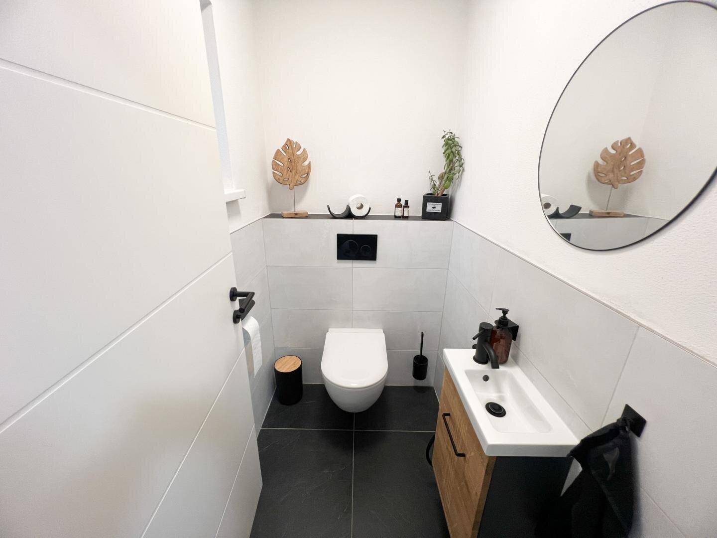Modernes Gäste-WC mit dunklen Bodenfliesen, Wand-WC und stilvollem Waschbecken.