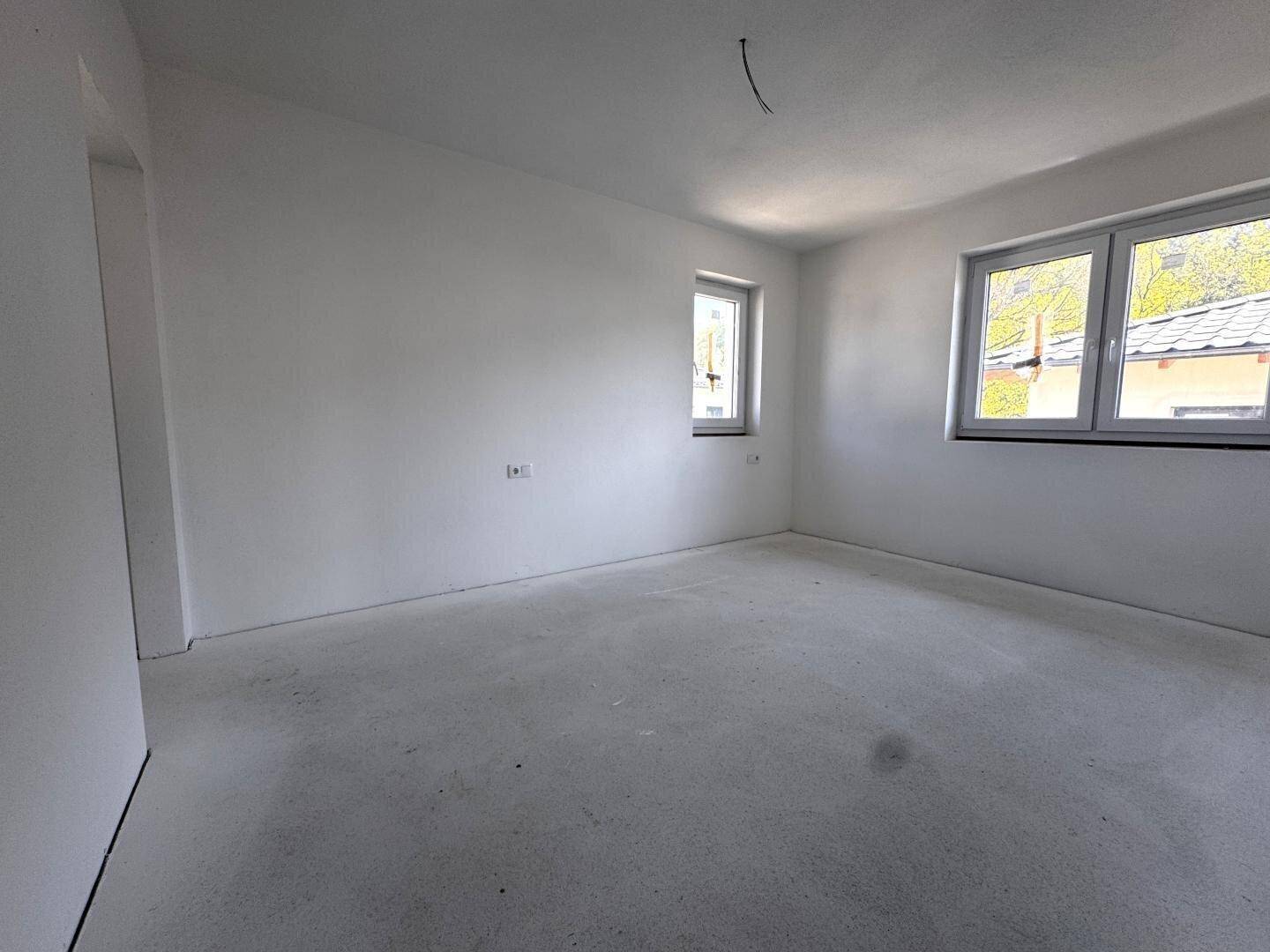 Unmöbliertes Zimmer im Rohbau mit zwei Fenstern, bereit für den Innenausbau.