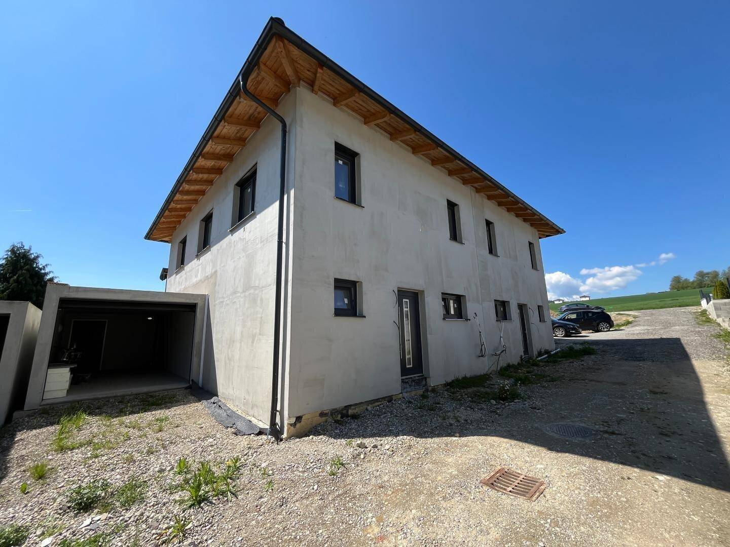Neubau-Doppelhaushälfte im Rohbau mit moderner Architektur, Carport und Zufahrt.