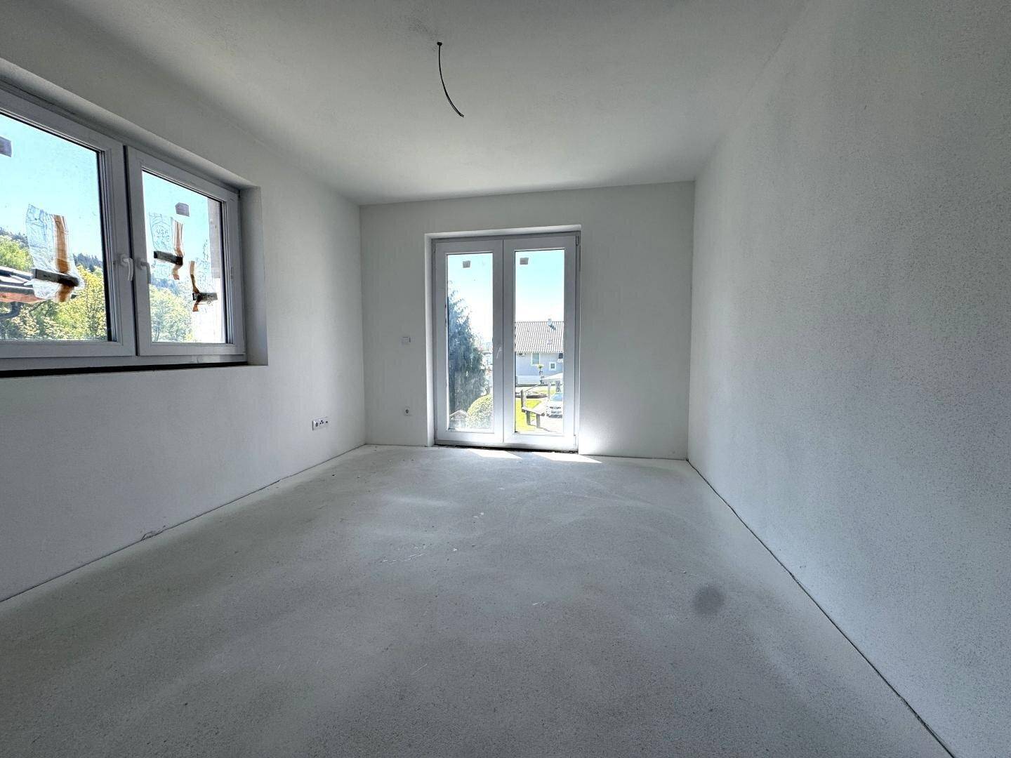 Helles Zimmer im Rohbau mit Fenster und Zugang zu einem möglichen Balkon oder Garten.