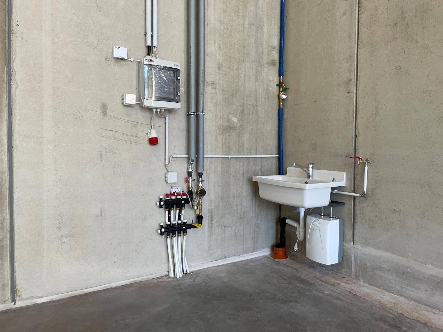 Eine Ecke eines Industrieraums mit sichtbaren Installationen, einem Waschbecken und einem Warmwasserbereiter.
