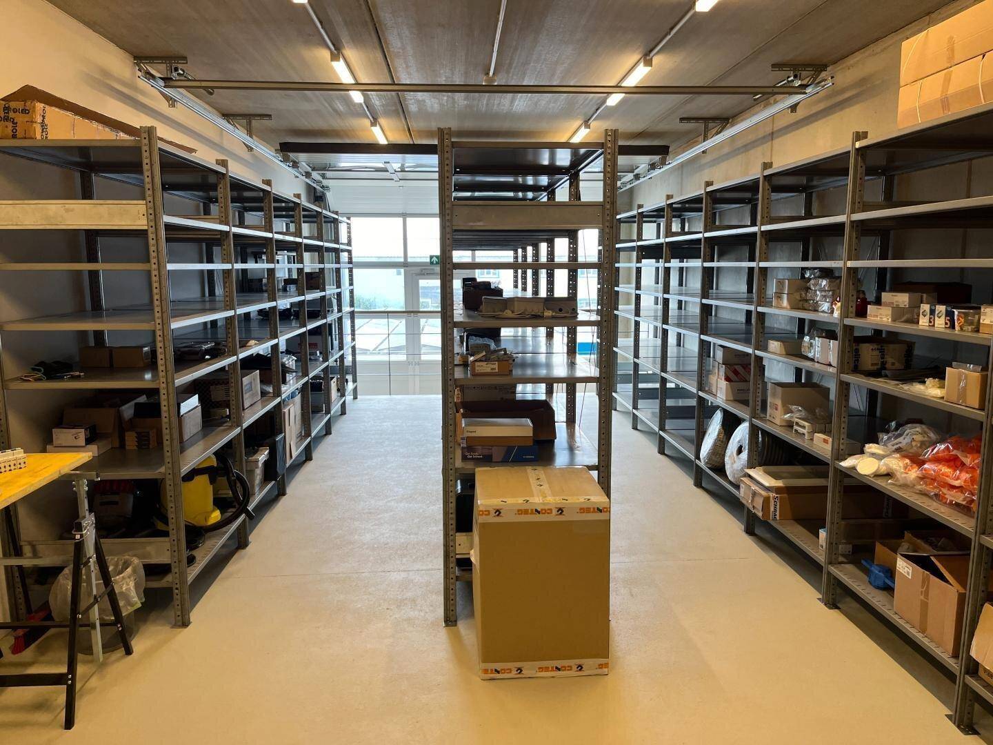 Organisiertes Lager mit Metallregalen, gefüllt mit Kartons und Materialien, unter einer hohen Decke.