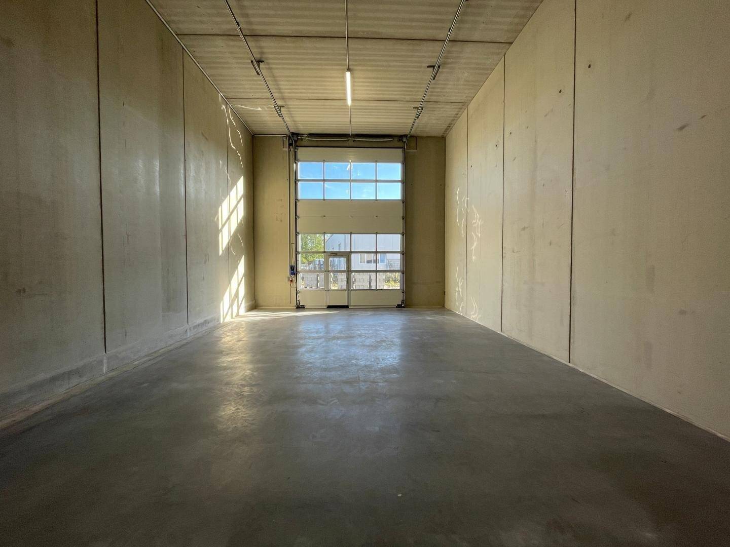 Geräumiger, leerer Lagerraum mit Betonwänden und einem großen Rolltor, das Tageslicht hereinlässt.