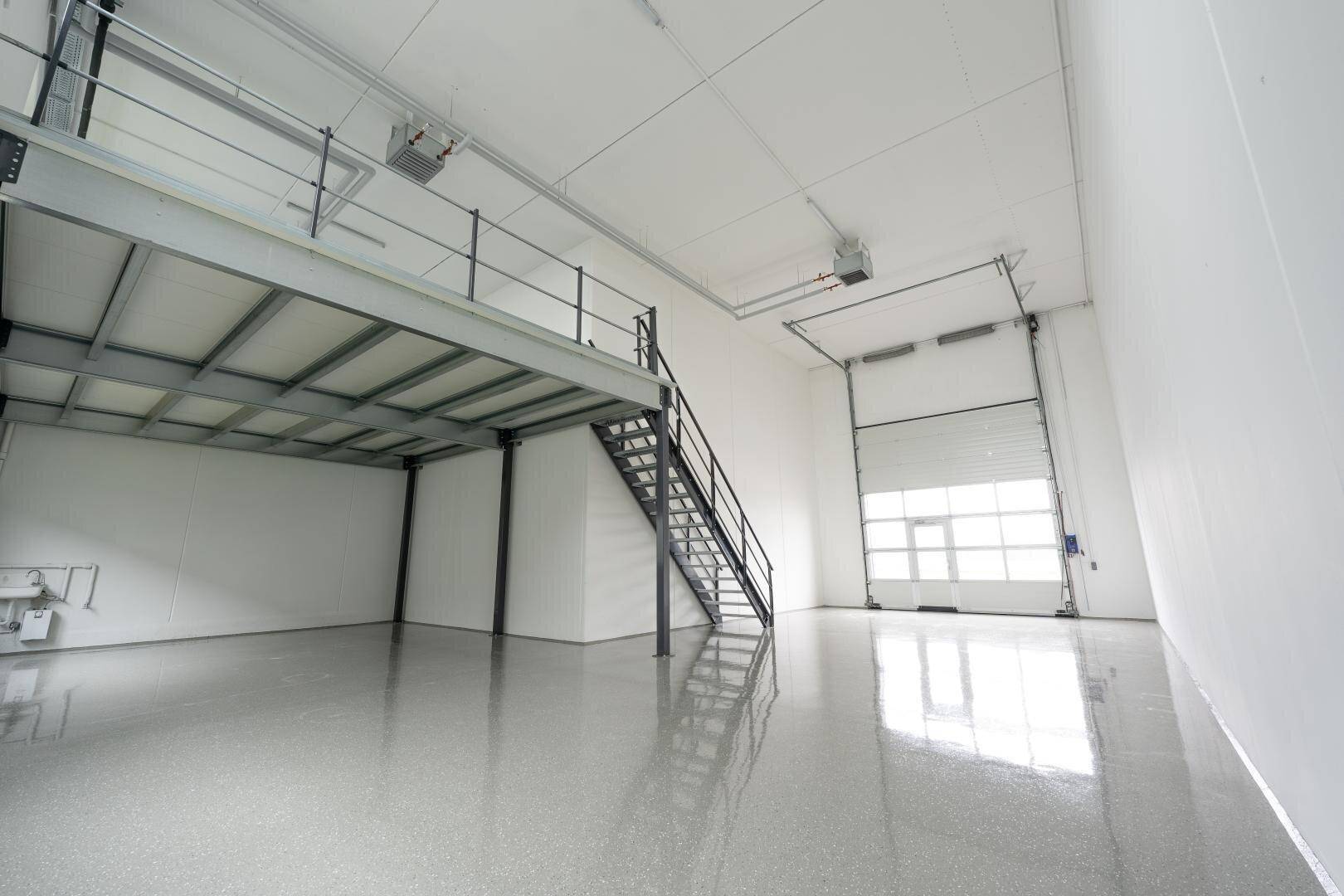 Heller, moderner Industrieraum mit glänzendem Boden, einer Stahltreppe und einer Mezzanine-Ebene.