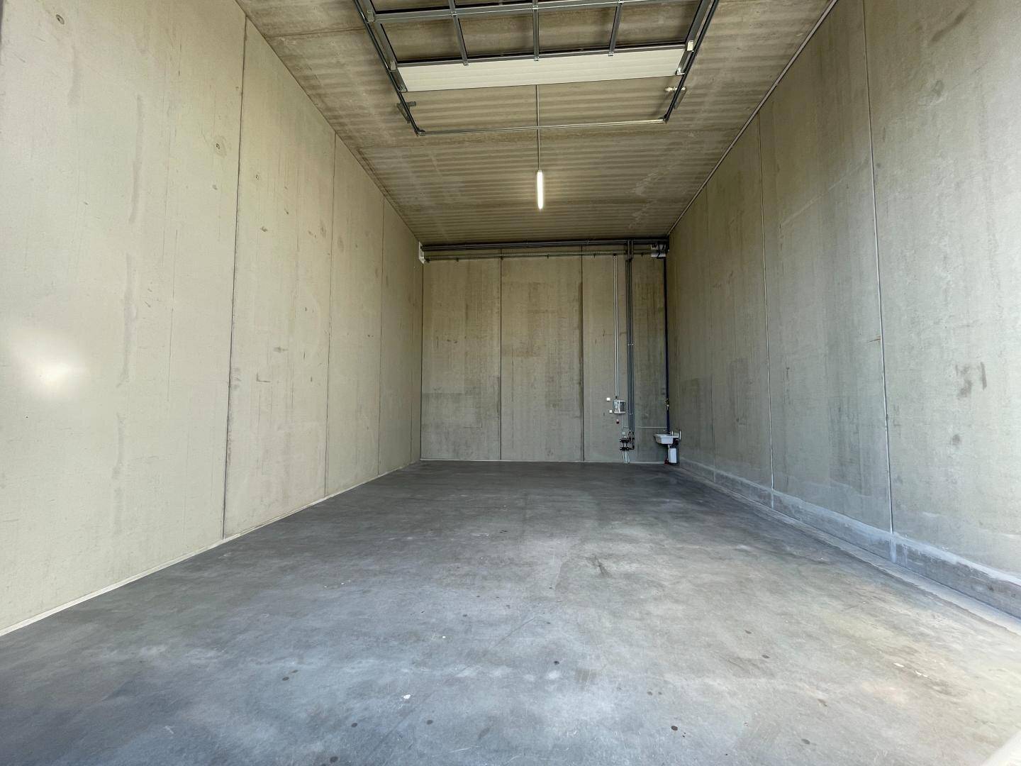 Geräumige, leere Lagerhalle mit hohen Decken, Betonwänden und glattem Betonboden, vielseitig nutzbar.