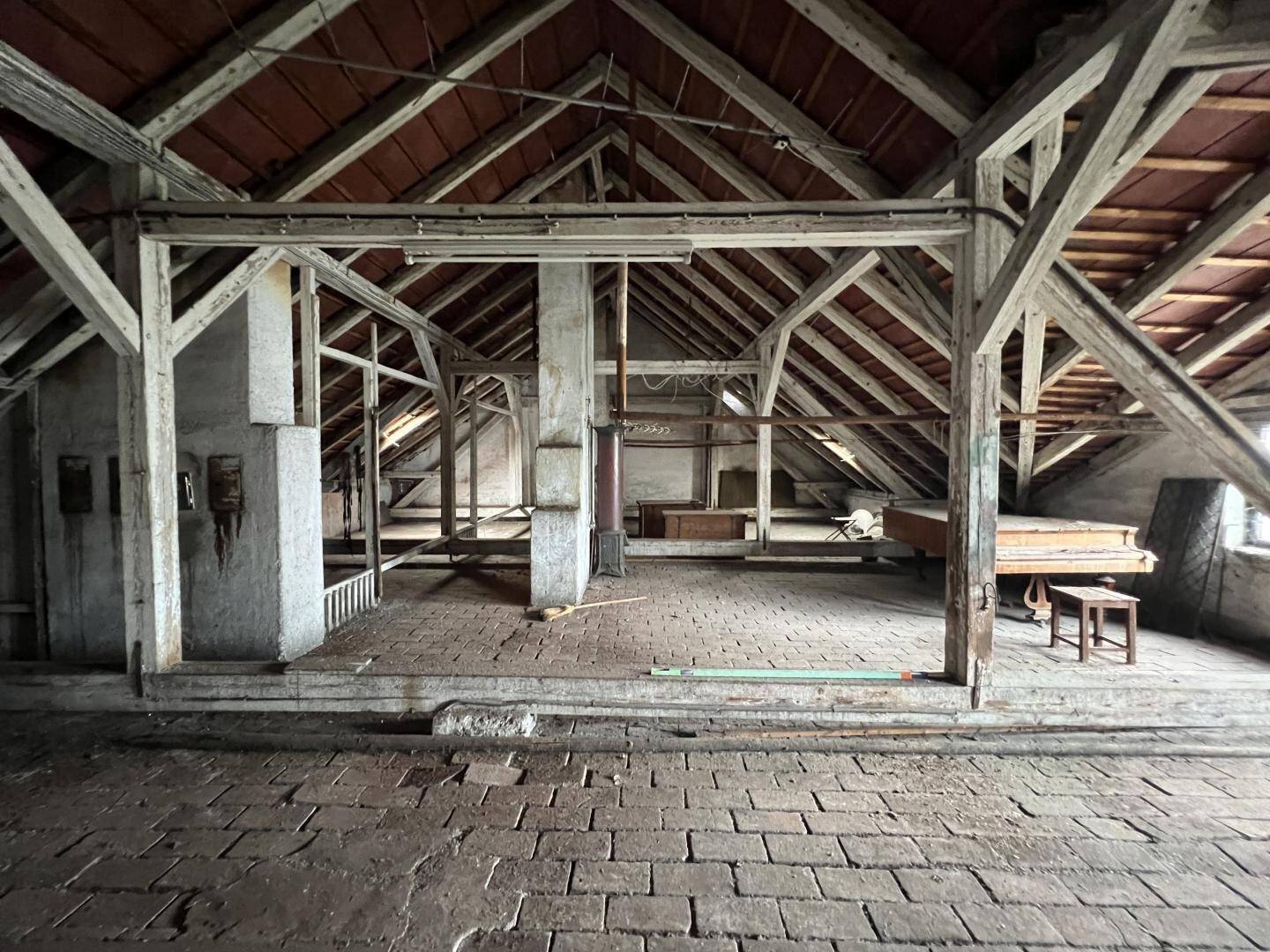 Geräumiger Dachboden mit sichtbaren Holzbalken und Ziegelboden, ideal für einen Ausbau.