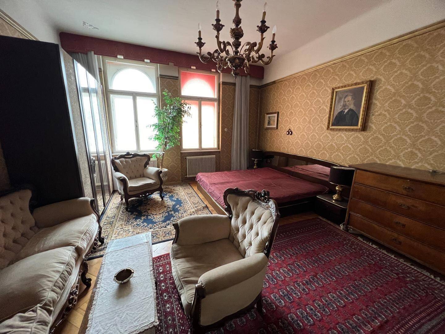 Klassisches Schlafzimmer mit opulenten Möbeln, gemusterter Tapete und einem Kronleuchter, der eine aristokratische Atmosphäre schafft.