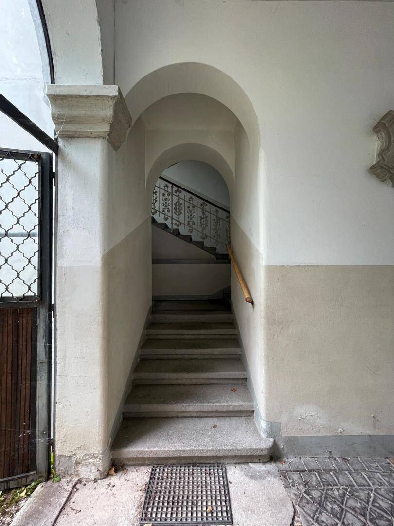Historisches Treppenhaus mit Stein- oder Betonstufen und einem verzierten Geländer, das nach oben führt.